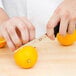 A person using a Victorinox serrated chef knife to cut an orange.