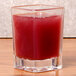 A Thunder Group plastic square shot glass with red liquid in it on a table.