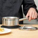 A chef holding a Vollrath stainless steel sauce pan with a lid on a stove.