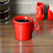 A red Fiesta china mug with a handle on a wooden table.