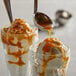 A spoon pouring I. Rice caramel topping over two glasses of ice cream.