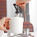A person using a Vollrath New York Coffee Urn with brass trim to pour coffee into a white mug.