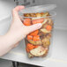 A hand holding a Solo MicroGourmet deli container of potatoes and carrots.
