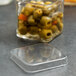 A clear plastic container with a American Metalcraft square PET lid on a glass jar filled with green olives.