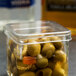 A close up of a container of American Metalcraft green jar lids over a jar of green olives.