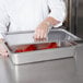 A chef using a Choice stainless steel cover on a large steam table pan to serve food.