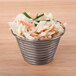 A stainless steel round ribbed sauce cup filled with coleslaw and green onions.