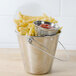 A stack of American Metalcraft stainless steel sauce cups filled with ketchup next to a bucket of french fries.