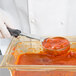A person in white gloves using a Vollrath black round portion spoon to serve red sauce.