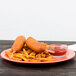 A plate of food with a Carlisle Sunset Orange melamine plate of hot dogs and french fries with a bowl of ketchup on the side
