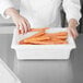 A chef cutting carrots into a white Rubbermaid food storage container.