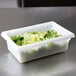 A white Rubbermaid food storage container filled with lettuce and green leaves.