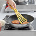 A hand using a spatula to cook meat patties in a Vollrath Optio non-stick frying pan.