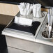 A Steril-Sil napkin and straw dispenser insert on a counter with silverware and napkins.