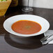 A CAC Majesty European bone china soup bowl filled with tomato soup on a table.