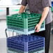 A Noble Warewashing 36-compartment gray full-size glass rack with four green extenders being handled by a person in a commercial kitchen setting.