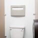 A white toilet with a Bobrick MatrixSeries seat cover dispenser installed on the wall above it.