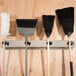 A Bobrick stainless steel mop and broom rack with four holders on a wall holding three brooms.