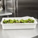 A white Cambro food pan filled with green lettuce on a kitchen counter.
