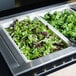 A white Cambro polycarbonate food pan filled with lettuce on a salad bar counter.