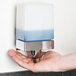 A hand using a Bobrick wall-mounted soap dispenser.