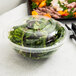 A clear Fineline plastic bowl filled with salad with a lid on top.