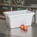 A white Cambro food storage box with a lid next to two apples.