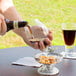 A person pouring a glass of brown liquid into a Libbey Belgian beer glass.