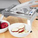 A Vollrath fruit slicer with a bowl of sliced apples and red apples.