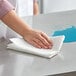 A hand wiping a counter in a professional kitchen with an Elegant 2-Ply paper towel.