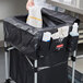 A woman holding a black Rubbermaid cover for a cart in a professional kitchen.