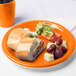 A Sunkissed Orange plastic plate with a sandwich and grapes on it.