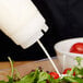 A person pouring white liquid from a Tablecraft Invertatop valve into a salad.