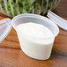 A Pactiv oval plastic souffle container filled with white sauce with a fork on top.