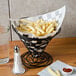A black wire cone basket filled with French fries on a table.