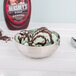 A round double wall stainless steel bowl of ice cream with chocolate toppings and a spoon.