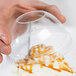 A hand holding a Dart clear plastic dome lid with a hole over a plastic cup with caramel on top.
