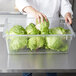 A chef holding a Rubbermaid clear polycarbonate food storage box of lettuce.