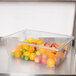 A Rubbermaid clear polycarbonate food storage box filled with fruit including apples and oranges.