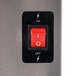 A red switch on a black rectangular panel over a silver surface.