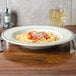A Homer Laughlin pasta bowl filled with spaghetti and sauce topped with parmesan cheese on a table with a glass of wine.