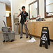 A woman mopping the floor with a Rubbermaid Executive Series black multi-lingual caution sign.