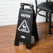 A Rubbermaid black and white caution sign on a wood floor.