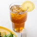 A Libbey Gibraltar stackable beverage glass filled with iced tea and a lemon slice on a table with a salad.