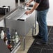 A man sliding a clear bottle with a white label into a Regency stainless steel lid on a counter over an ice bin.