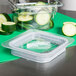 A clear plastic Cambro food pan lid with slices of cucumbers inside.
