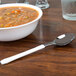 A bowl of soup on a table with a WNA Comet white plastic teaspoon.