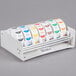 A white Noble Products dispenser rack holding seven rolls of food labeling stickers.