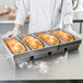 A person in a white chef's uniform holding a tray of bread loaves baked in a Chicago Metallic 4-Strap Bread Loaf Pan.