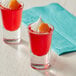 Two Acopa shot glasses filled with red and orange juice on a counter.
